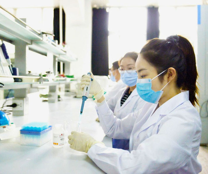 Scientists in lab coats and masks conduct experiments using pipettes in a bright, modern laboratory setting.