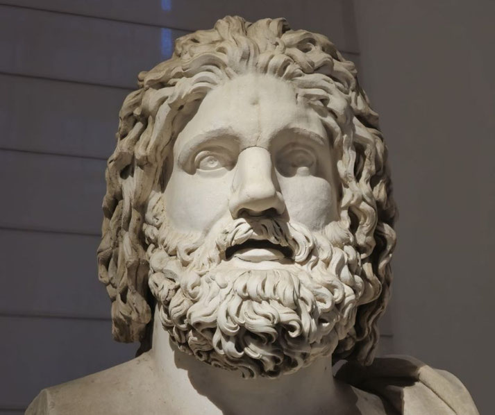 Close-up of a marble statue showing a bearded man with long, wavy hair and an intense, upward gaze.