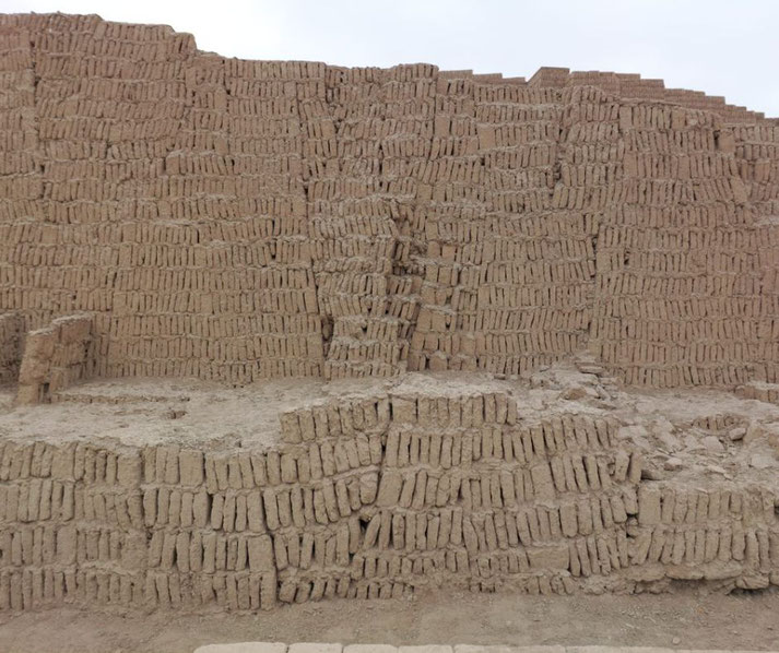 An ancient adobe wall at Huaca Pucllana in Lima, Peru. The clay bricks are stacked vertically in a "bookshelf" style, showing signs of erosion and wear over time.