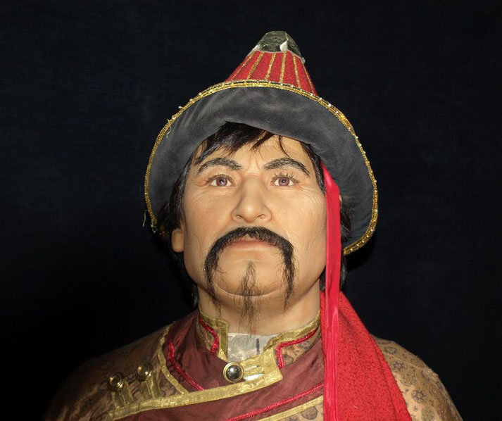 A lifelike wax figure of a Mongolian warrior or nobleman wearing a traditional hat with gold trim and a red tassel.
