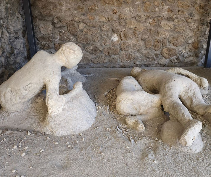 Two plaster casts of victims from Pompeii, one kneeling and one lying face down, preserved in volcanic ash.