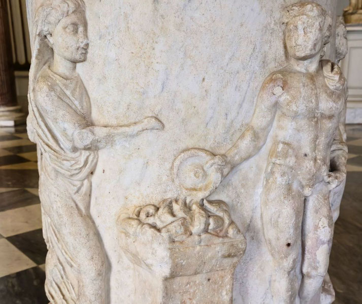 Relief sculpture of a woman and a man near an altar with offerings; the man holds a circular object, possibly a dish, in a ritual or ceremonial scene.