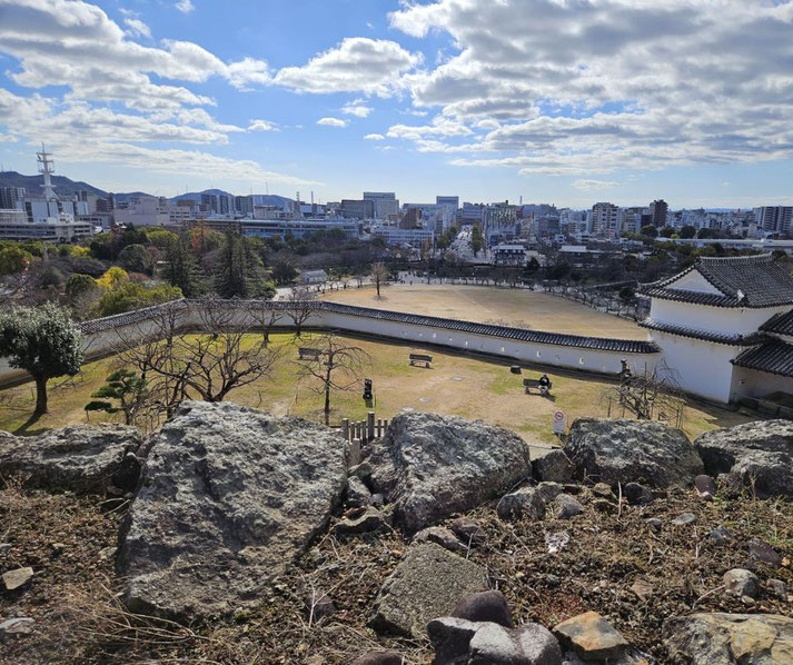 A scenic view from Himeji Castle overlooking its outer grounds, stone walls, and a park with trees and benches.