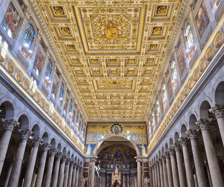 The interior of the Basilica of Saint Paul Outside the Walls features a gilded coffered ceiling, towering marble columns, and vibrant mosaics, creating a grand and ornate sacred space.