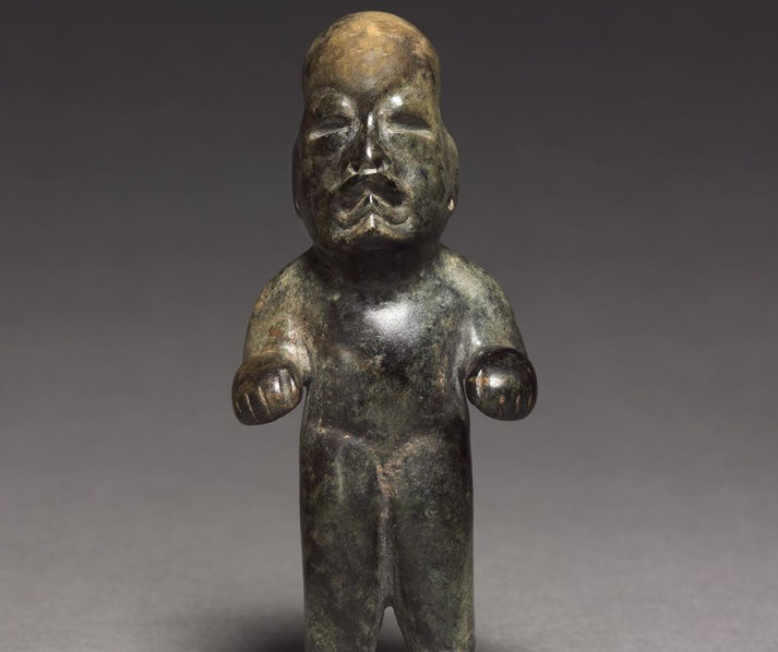 A small, dark green stone figurine with a rounded head, minimal facial features, and short limbs.
