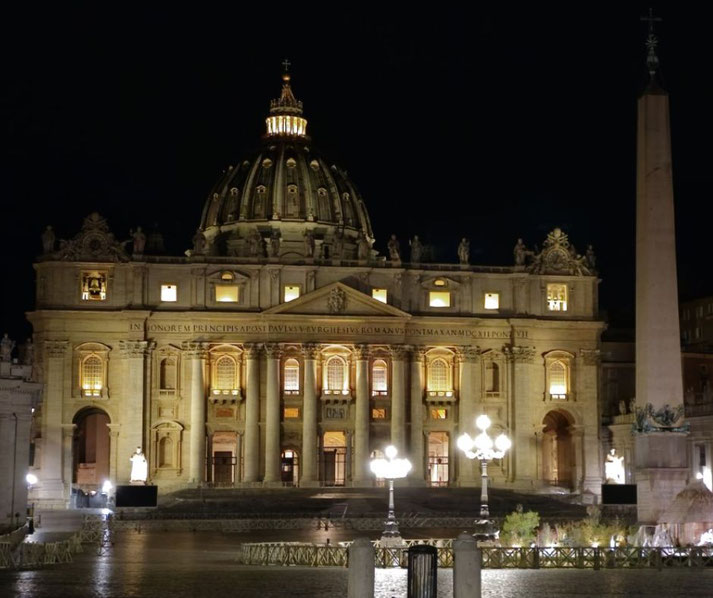 St. Peter’s Basilica at night, illuminated with warm lights highlighting its grand dome, columns, statues, and the Vatican obelisk in St. Peter’s Square.