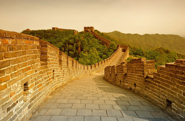 Great Wall of China stretching over lush green hills, with its brick pathways and battlements glowing under a warm, golden light in a serene and timeless landscape.