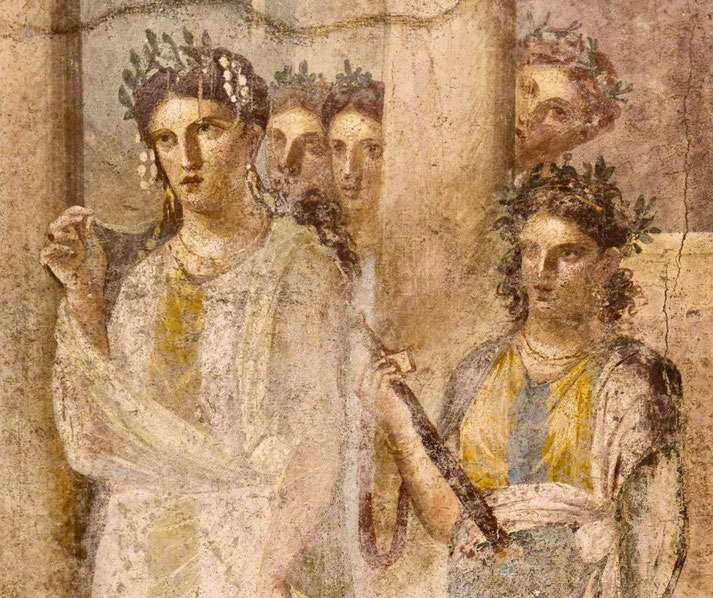 Ancient fresco of women in laurel wreaths, one holding a staff and another lifting her garment, with several partially hidden figures in the background behind a column.