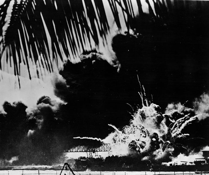 A massive explosion erupts at a naval base, lighting up the night sky with fire and smoke as palm fronds frame the foreground.