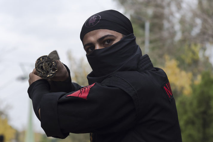 A ninja dressed in black holds a katana in a defensive stance.