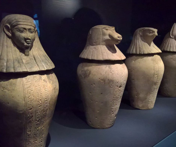 Four ancient Egyptian canopic jars, each with a unique lid representing the Four Sons of Horus. These jars, inscribed with hieroglyphs, were used to store mummified organs for the afterlife.