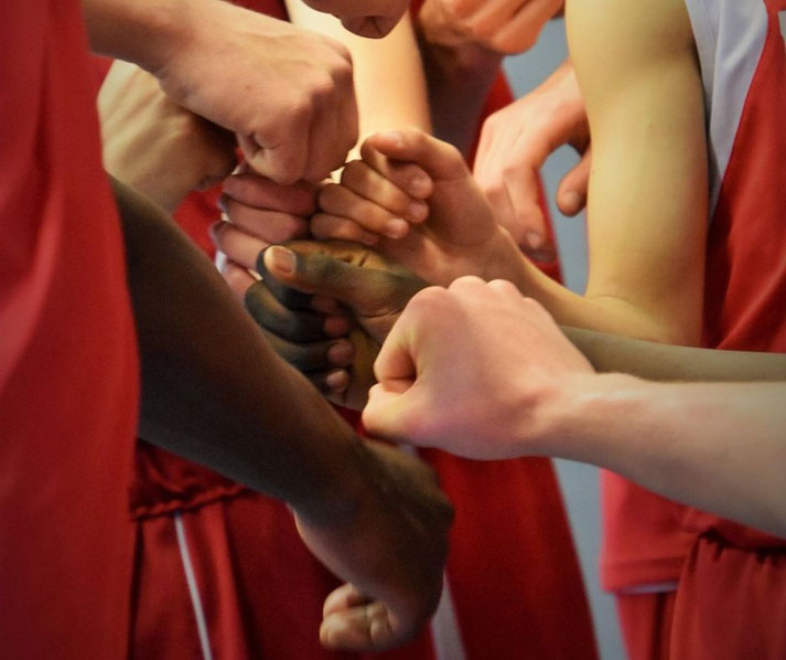 A group of basketball players in red jerseys join fists together in a huddle before a game.