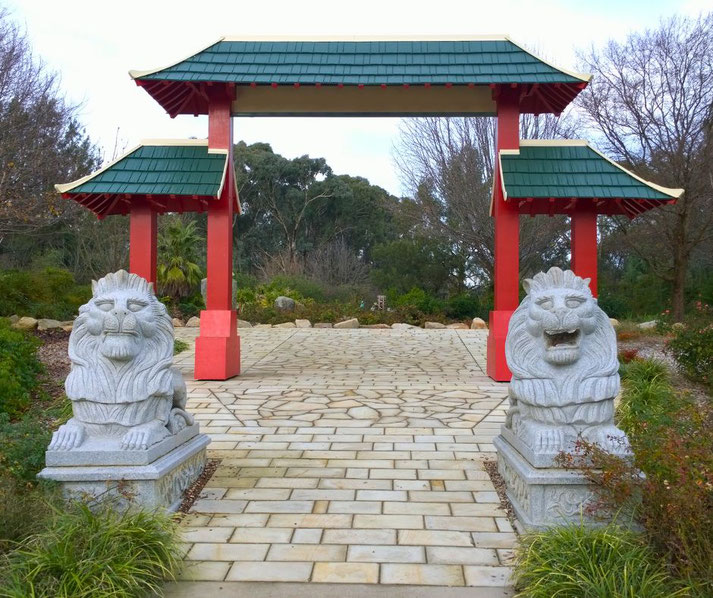 A traditional Chinese-style gateway with red pillars and a green-tiled roof, flanked by two stone lion statues.