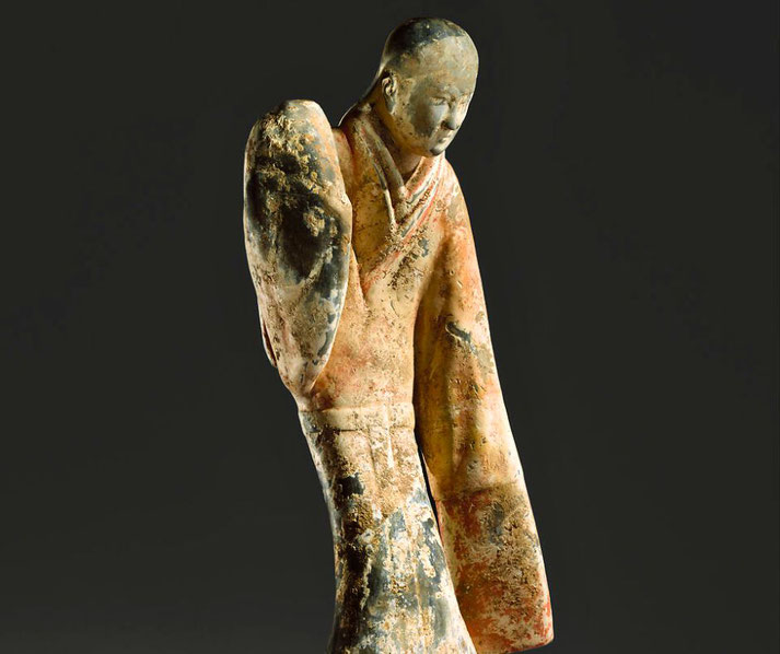 An ancient Chinese terracotta figurine of a female dancer. She wears flowing robes with faded pigments and poses gracefully.