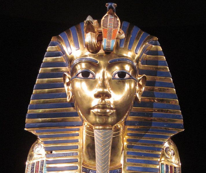 The funeral mask of Tutankhamun, made of gold with inlaid blue and red details. It features the Nemes headdress, a cobra and vulture, and intricate craftsmanship symbolizing royalty.