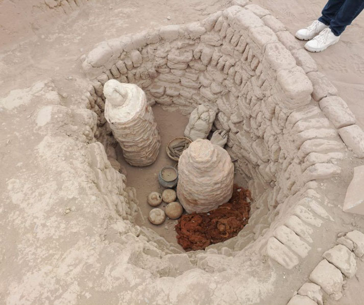 An excavated burial site at Huaca Pucllana in Lima, Peru. It contains wrapped mummies, ceramic vessels, and other artifacts.