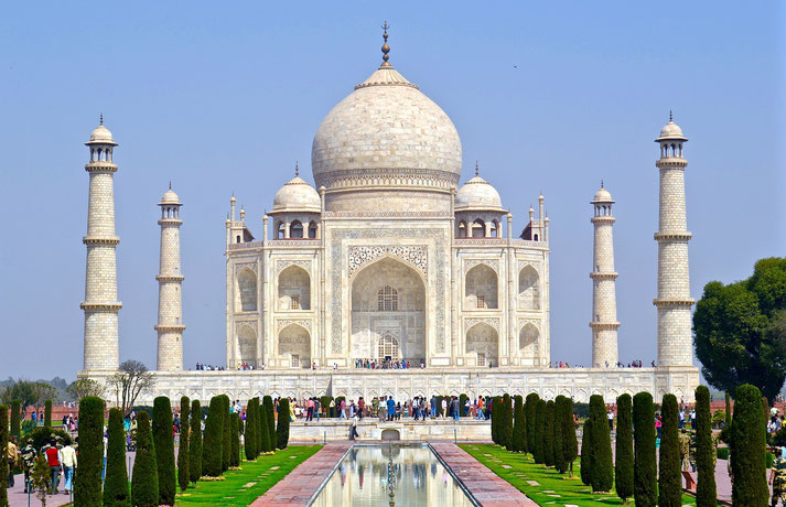 Taj Mahal in Agra, India, showcasing its iconic white marble dome, symmetrical minarets, and reflecting pool surrounded by manicured gardens under a clear blue sky.