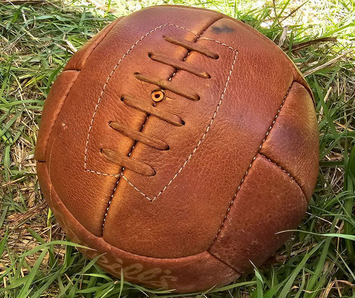 Vintage leather football with visible stitching and laces, resting on grass.