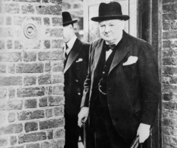 Winston Churchill is seen entering No. 10 Downing Street by the back door during World War II, wearing a dark suit and hat