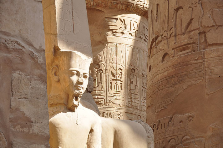 Close-up of an ancient Egyptian statue beside hieroglyph-covered stone columns bathed in warm sunlight.
