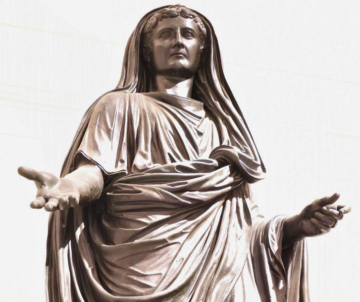 Bronze statue of a robed figure with a veil over the head, arms extended in a gesture of offering or speech, exuding authority and calm.