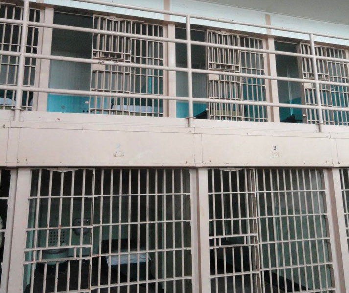 Two levels of barred prison cells are visible, each with metal doors and sparse interiors, part of an older correctional facility.