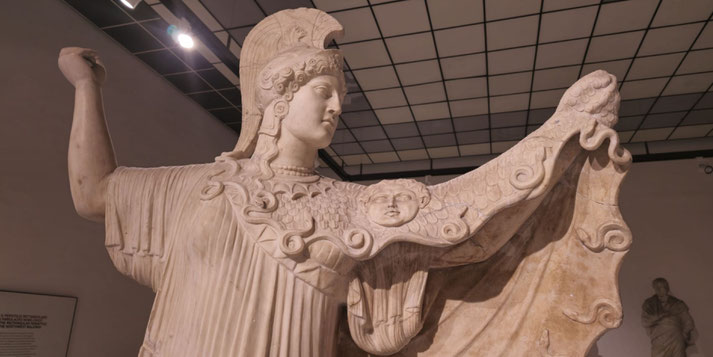 Marble statue of Athena in a plumed helmet, raising her cloak adorned with the Gorgon's head and snake motifs, symbolizing protection and divine power.