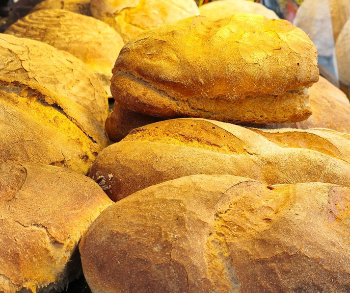 A close-up of golden-brown artisan bread loaves with crispy crusts, arranged in a display, highlighting their rustic texture and freshly baked appearance.