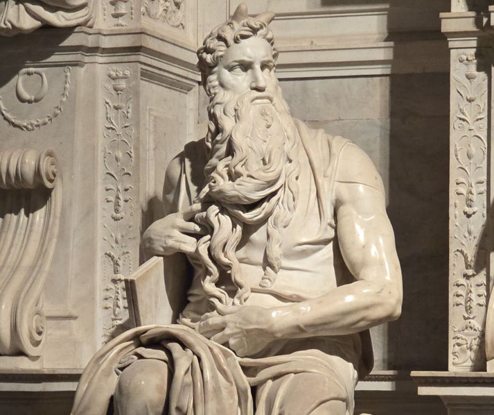 Michelangelo's marble statue of Moses, seated with a long flowing beard, muscular arms, and small horns on his head, holding tablets, part of a richly decorated architectural setting.