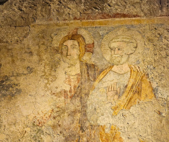 Wall painting in Mamertine Prison showing worn figures with halos, set against textured stone, hinting at early Christian presence in the ancient site.