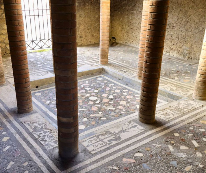 Ancient Roman room with brick columns and a decorative mosaic floor featuring geometric and floral patterns in a central sunken area.