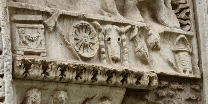 Detailed stone carving featuring a bull’s head, rosette, and various symbolic objects, likely part of an ancient Roman frieze or altar decoration.