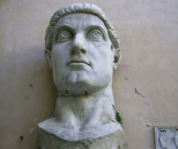 Massive marble head of a Roman emperor with wide eyes and defined features, set against a plain wall.