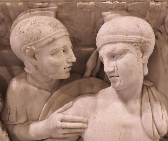 Marble relief showing two ancient warriors in helmets, one touching the other's shoulder in a moment of solemn connection.
