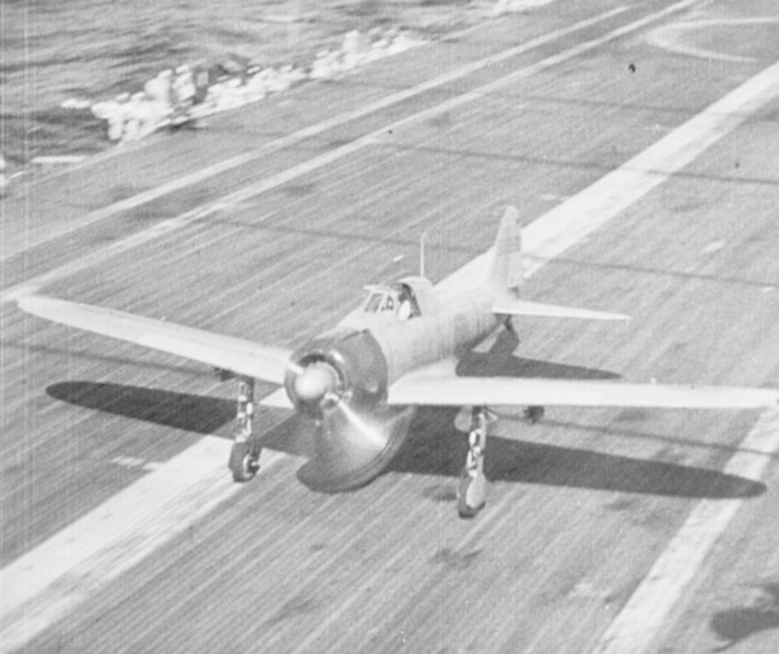 A military aircraft with spinning propeller prepares for takeoff from an aircraft carrier's deck during wartime.