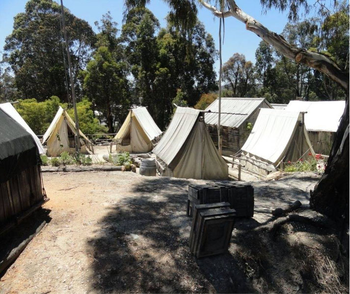 A historical tent settlement, possibly a gold rush-era camp, with canvas tents, wooden huts, and scattered crates.