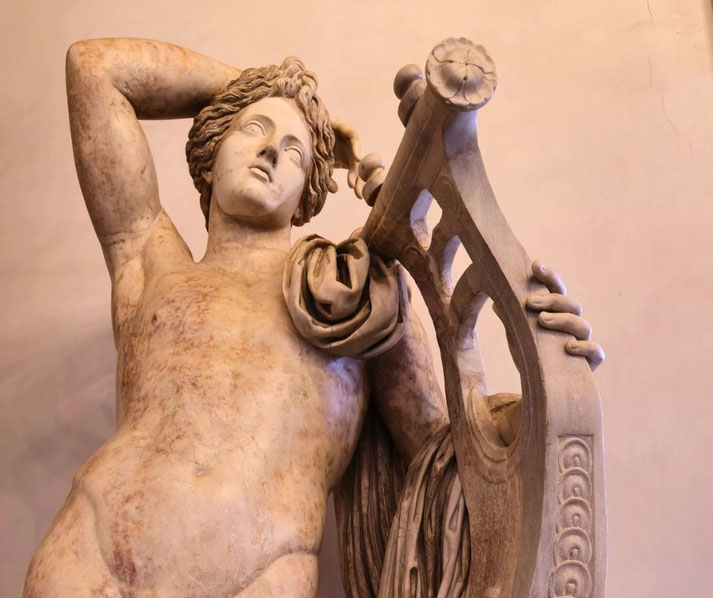 Marble statue of a relaxed, partially draped figure leaning on a large lyre, gazing upward with a dreamy expression.