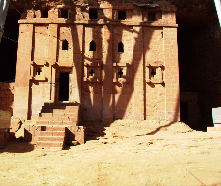 Facade of a rock-hewn church with geometric windows and a central staircase carved into red stone in Ethiopia.