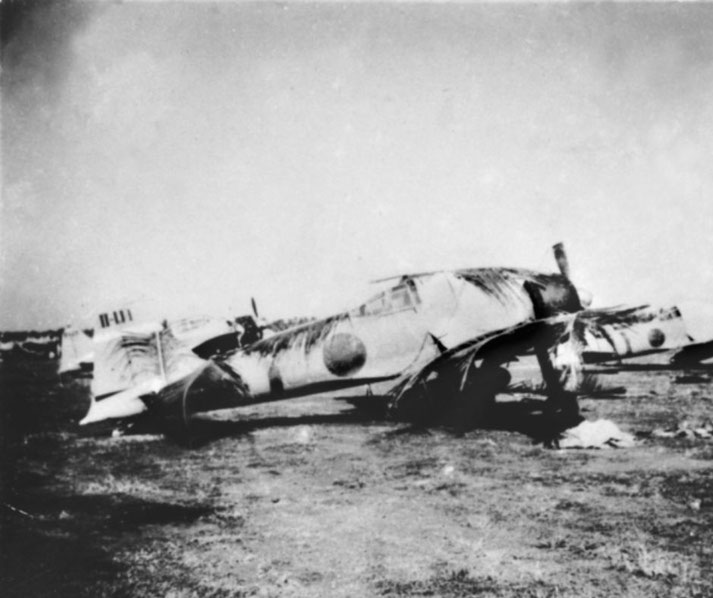 A heavily damaged Japanese fighter plane lies wrecked on the ground, its fuselage and wings scorched.