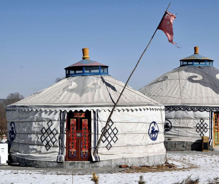 Two traditional Mongolian yurts with decorative patterns stand under a clear blue sky. 