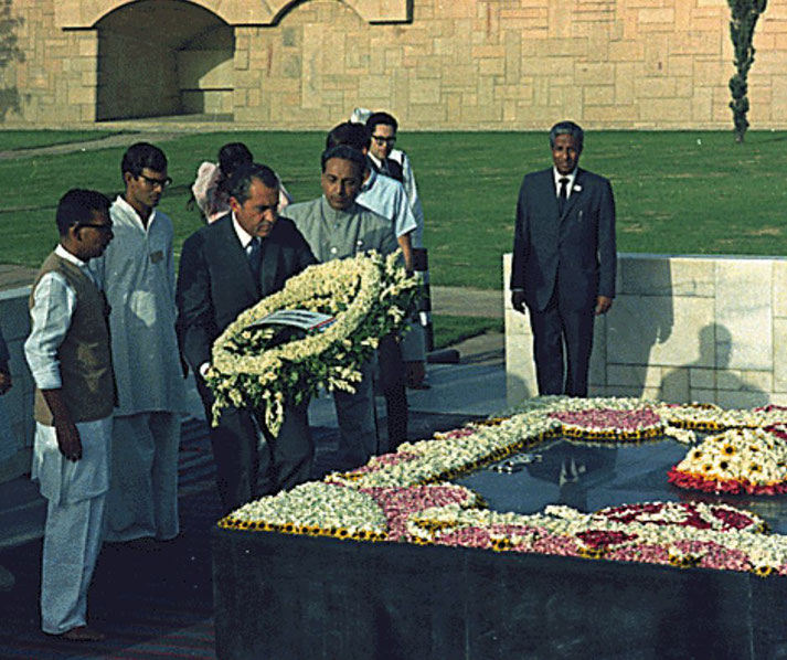 A group of men, including Richard Nixon, lay a floral wreath at a flower-covered black marble memorial site in an outdoor setting.