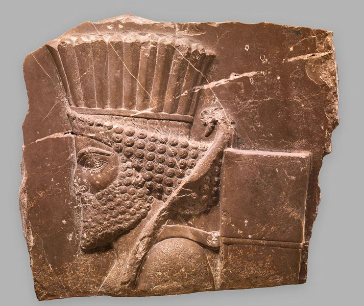 Ancient stone relief of a Persian figure in profile, featuring a detailed beard, ornate headdress, and quiver with arrows.