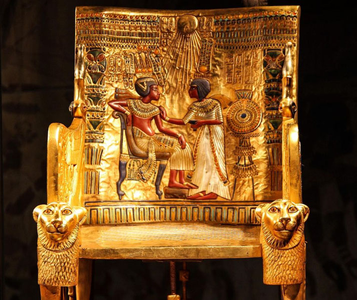 Tutankhamun's golden throne, richly decorated with intricate carvings. The backrest features a scene of the pharaoh and his queen, with Aten's rays shining down, symbolizing divine favor.