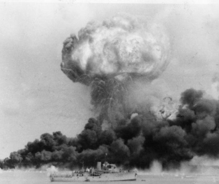 A massive explosion sends a mushroom cloud skyward as thick smoke engulfs a ship near the blast site.