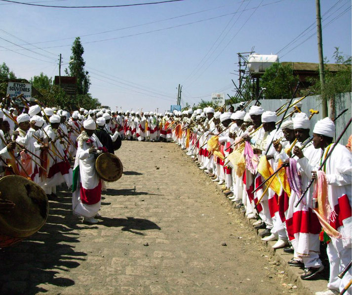 A large group of Ethiopian men in traditional white clothing play instruments and gather for a cultural or religious procession.