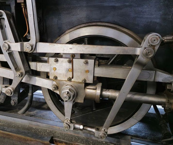 A detailed view of a locomotive's metal driving wheels and connecting rods, showcasing intricate engineering. The polished steel components highlight the mechanics of the steam engine's propulsion system.