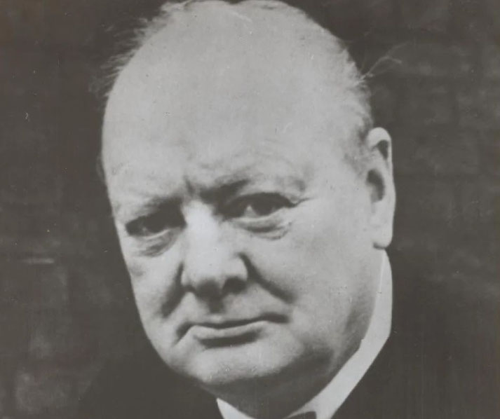 A black-and-white close-up of an older man with a stern expression, bald head, and formal attire, facing the camera directly.