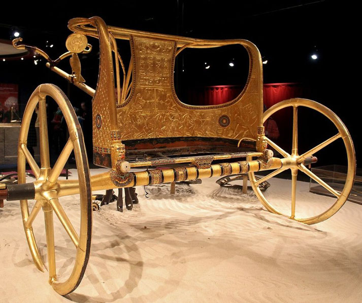 A replica of an ancient Egyptian chariot, gilded and intricately decorated. It features six-spoked wheels, ornate carvings, and symbolic motifs, reflecting its royal and ceremonial use.