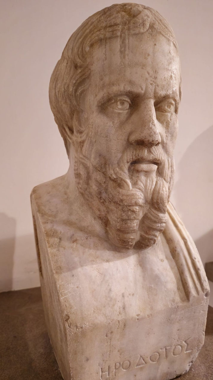 Marble bust of a bearded man with wavy hair and intense gaze, featuring Greek inscription “ΗΡΟΔΟΤΟΣ” carved at the base.