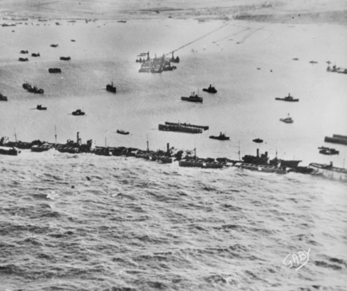 Aerial view of numerous ships and landing craft off a crowded WWII invasion beachhead, preparing for amphibious operations.